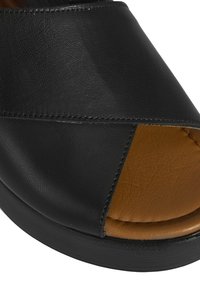 Schwarze Ledersandale mit offenem Zeh, ausgestattet mit einem Kreuzriemen-Design und einem tanfarbenen Innenbereich. Die Sohle besteht aus einem glatten schwarzen Material.