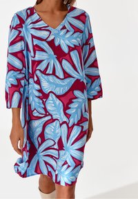 V-kaulus, polven mittainen tunikamekko, jossa on kirkas sininen lehtikuvio viininpunaisella taustalla, valmistettu kevyestä kankaasta. Kolme neljäsosapituista hihoista.