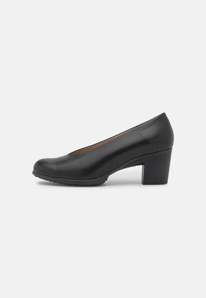 Chaussure à talon en cuir noir avec un bout arrondi et un talon bloc de hauteur moyenne. Texture lisse avec un léger éclat et aucune décoration visible.