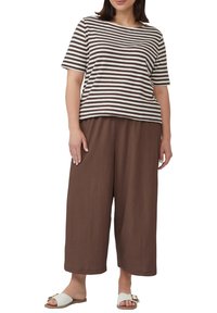Gestreiftes braun-weißes Kurzarmoberteil kombiniert mit braunen weit geschnittenen Hosen. Das Model trägt weiße Riemchensandalen mit einer dekorativen Schnalle.
