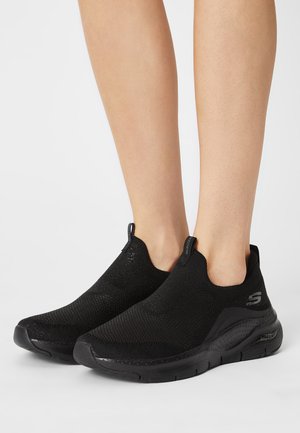 Black slip-on shoes made of textured knit material, featuring a lightweight midsole, rounded toe, and contrasting logo on the side.