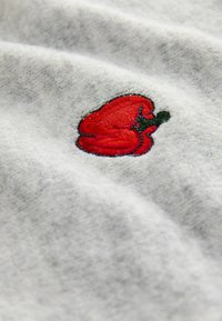 Tessuto grigio con una superficie testurizzata che presenta un peperone rosso ricamato con accenti verdi. Il design è dettagliato e vivido.
