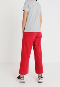 Czerwone spodnie z korduroy o prostym kroju nogawki, zestawione z szarym t-shirtem oraz czarno-różowymi butami sportowymi. Tekstura jest żeberkowana.