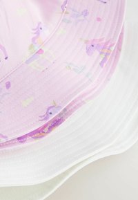Chapeaux seau en rose avec des motifs de licornes et options en coton blanc. Présente des bords incurvés et des détails cousus. Tissu texturé.