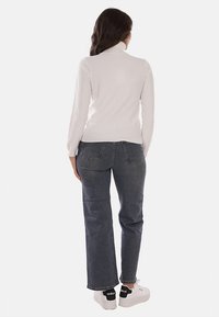 Maglione bianco a maniche lunghe con collo alto abbinato a jeans scuri a vita alta con gamba dritta e sneakers bianche con dettagli neri.