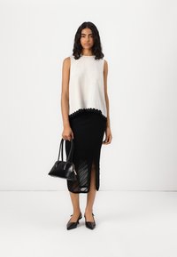 Top sans manches blanc avec un bas festonné, associé à une jupe midi noire côtelée avec une fente sur le côté, un sac à main noir et des ballerines pointues.