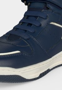 Gros plan d'une basket en cuir bleu marine avec des lacets assortis et une semelle blanche avec grip texturé.