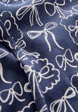 Tmavě modrá texturovaná látka s bílými květinovými a mašličkovými vzory, vytvářející bohatý kontrast s hmatovou povrchovou úpravou a výraznými designovými prvky.