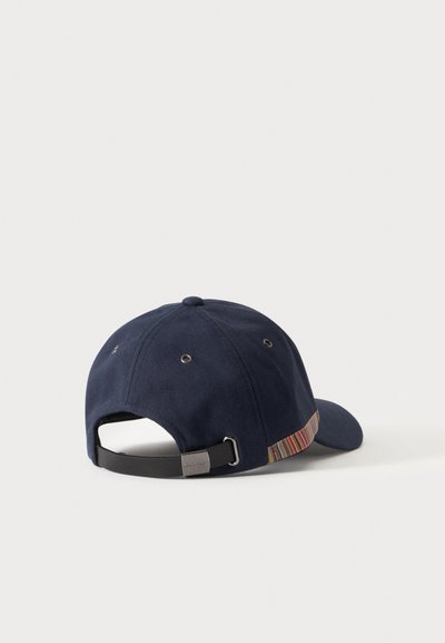 Casquette de baseball bleu marine avec une sangle métallique ajustable et un détail rayé multicolore sur le côté, montrée de dos sur un fond uni.
