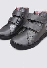 Bottines pour enfants grises avec double bande velcro et accents à motif serpent brillant, doublure intérieure rose et semelles noires.