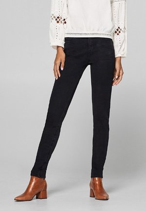 Schwarz elegante Slim-Fit-Jeans, kombiniert mit braunen Stiefeletten mit Absatz und einer weißen Langarmbluse mit Lochstickereien.