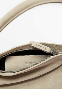Beige suede handbag with partially open silver zipper revealing interior and embossed brand name on inner pouch.