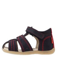 Sandalia azul oscura con costuras rojas, correa de velcro, diseño abierto, suela de goma y perforaciones para transpirabilidad. Apta para niños.