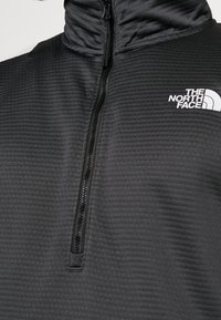 Pullover a mezza zip di colore nero, realizzato in tessuto testurizzato. Presenta un colletto alto e un logo bianco a contrasto sul petto.