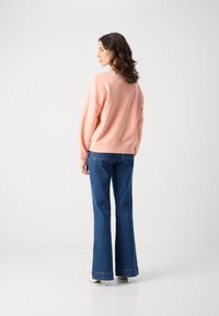 Støvet rosa genser med lange ermer, avslappet passform og ribbestrikkede mansjetter, sammen med mørkeblå jeans med utsvingte ben og brettede hems.