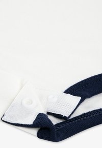 Λευκό ένδυμα με γιακά σε ναυτικό μπλε και λεπτομέρειες με κουμπιά, με απαλή βαμβακερή υφή και αντίθετες ραφές.