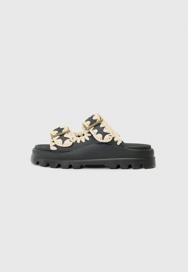 Sorte sandaler med to brede stropper med kremfargede vevde detaljer og en teksturert såle. Flat profil med en kraftig, rillede base.