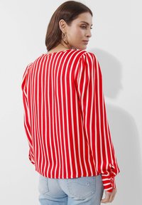 Rot-weiß gestreifete Bluse mit langen Ärmeln, Puff-Schultern, rundem Halsausschnitt und Knopfärmeln, getragen mit hellblauen Jeans.