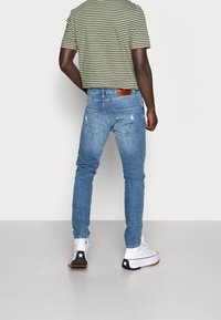 Tunna blå jeans med slitna detaljer vid bakfickorna, matchade med en grön och vit randig t-shirt med korta ärmar och högskurna sneakers.