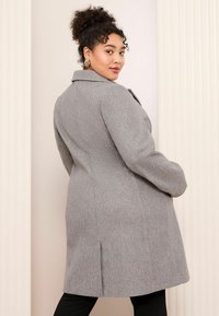 Manteau en mélange de laine gris avec un col cranté, des manches longues et des fentes latérales, doté d'un design structuré et d'une texture lisse.