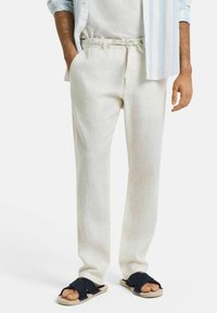 Lichtbeige linnen broek met een taillekoord, zijzakken en een relaxte pasvorm; gecombineerd met donkerblauwe sandalen. Glad textuur.