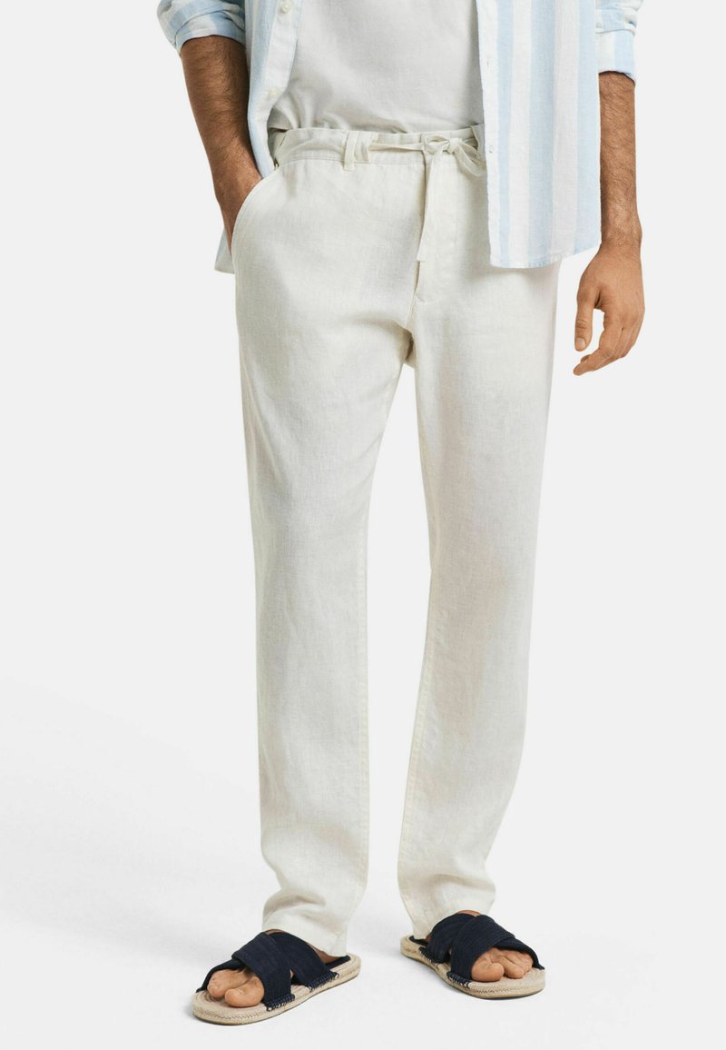 Lichtbeige linnen broek met een taillekoord, zijzakken en een relaxte pasvorm; gecombineerd met donkerblauwe sandalen. Glad textuur.