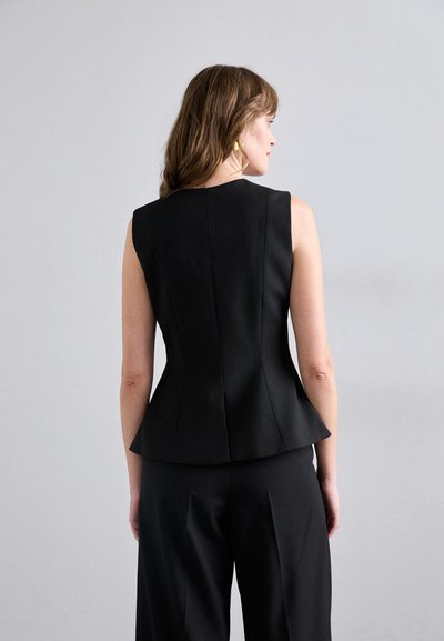 Svart ermeløs topp med tettsittende bodice, utvidet peplum og subtile sømmer. Glatt stoff uten synlige mønstre eller hardwaredetaljer.