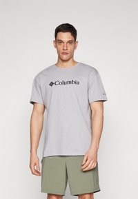 Šedé tričko s krátkým rukávem, na přední straně s černým logem "Columbia", vyrobené z bavlny, s kulatým výstřihem a volným střihem.