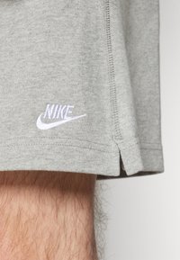 Primer plano de la pierna de una persona que lleva pantalones cortos grises de Nike con el logo blanco de Nike visible y detalles en la costura lateral.