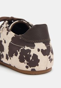 Sneaker im Kuhmuster mit einem beige-braunen Lederoberteil, abgerundeter Ferse und brauner Gummisohle. Mit gesteppten Akzenten und Schnürverschluss.