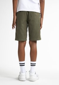 Khaki shorts met een rechte snit, zichtbare zakken, gecombineerd met witte gestreepte sokken en witte sneakers, weergegeven vanuit een casual achteraanzicht.