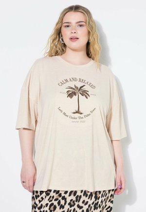 Beige oversized t-shirt lavet af blødt stof med et palmetræ grafik og tekst: "Rolig og Afslappet" og "Lad os Mødes Under Palmetræerne."