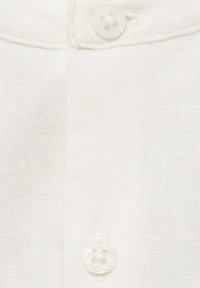 Tessuto di lino bianco con una vista ravvicinata di un bottone da cucire con un design floreale, che mostra una fine trama e una leggera trasparenza.