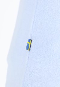 Ljusblå fleece tyg med en mjuk textur, som har en liten svensk flagga i blått och gult på sömmen.