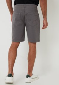 Grå shorts med lige snit, bæltesløjfer og to baglommer med syede accenter. Båret med hvide sneakers med mørkegrønne hæl-tabs.