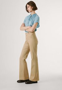 Ljusblå blus med korta ärmar och volangkrage, parat med beige utsvängda byxor och svarta skor. Enfärgade, släta tygtexturer.