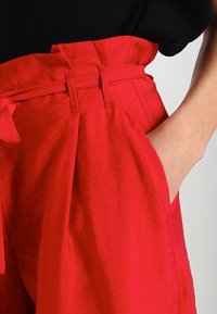 Rote Hose mit strukturiertem Finish, hoher Taille und gebundenem Gürtel, seitlichen Taschen und lockerer Passform.