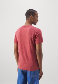 T-shirt vermelho de manga curta com decote redondo, textura suave e um corte descontraído, utilizado com jeans de ganga azuis.