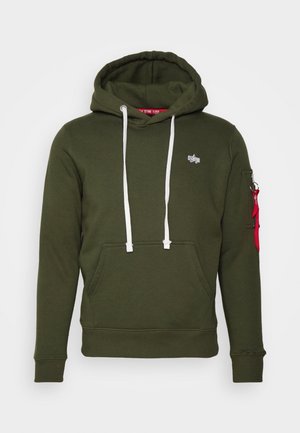 Ciemnozielona bluza z kapturem z białymi sznurkami, przednia kieszeń kangurka, małe logo na piersi oraz kieszeń na rękawie na zamek z czerwoną tkaninową pętelką.