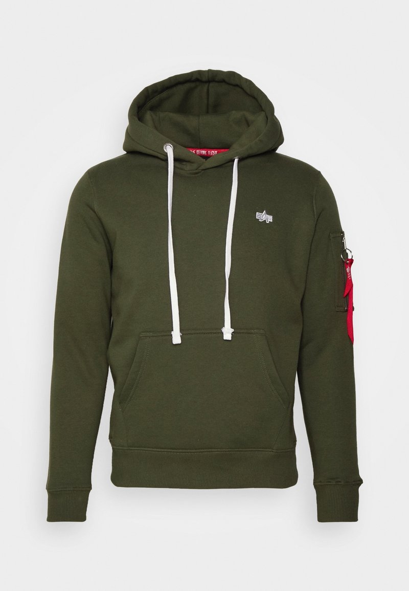 Sweat à capuche vert foncé avec cordons blancs, poche kangourou devant, petit logo poitrine et poche zippée sur la manche avec tirette en tissu rouge.