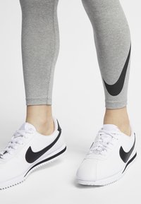 Grey athletic leggings with a black Nike swoosh design, paired with white sneakers that feature a black accent and textured sole.