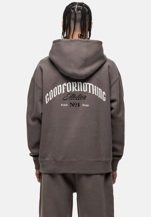 Graue, oversized Kapuzenjacke mit einem großen weißen Grafiktext auf dem Rücken, gerippten Bündchen und einer Kängurutasche. Hergestellt aus weichem, strukturiertem Stoff.