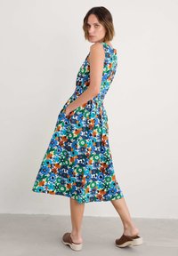 Rochie midi florală cu un corset ajustat, fundal vibrant albastru, flori verzi, portocalii și albe, și buzunare laterale. Prezintă o fustă evazată.