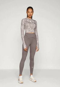 Hallide mustriga pikakäiseline topp ja kõrge vöökohaga leggingid, millel on tekstureeritud kangas ja sobiv disain, koos valgete sportlikekingadega.