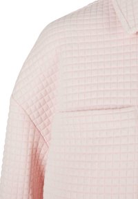 Tissu matelassé rose clair avec détail de couture carrée sur l'épaule, la manche et la zone de la poche poitrine d'un vêtement.