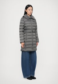 Hall hall talvejope kunstkarusnahast kraega, vööga vöökohal ja horisontaalse tikandiga. Kandmise all laia säärega teksapüksid ja pahkluu saabad.