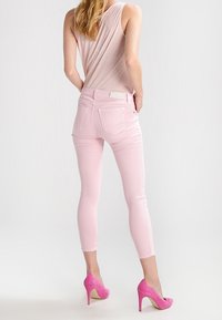 Mujer vestida con top sin mangas rosa claro, pantalones cortos ajustados rosa claro y tacones altos rosa brillante, de pie con la espalda hacia la cámara.