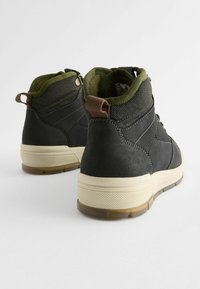 Czarne i zielone wysokie buty sportowe z teksturowaną skórzaną i materiałową cholewką, z brązowym akcentem na języku oraz gumową podeszwą z detalami poprawiającymi przyczepność.