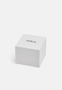 Baltas kvadratinis degtukas su lygiu paviršiumi. Viršuje yra juodu raštu atspausdinta tekstas "FURLA" ir "SINCE 1927 ITALY". Paprastas dizainas be papildomų akcentų.