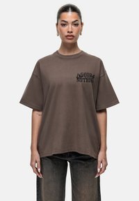 Bruine oversized t-shirt van zacht katoen, met een zwarte grafische print die "GOOD FOR NOTHING" leest op het linkerborstgebied.